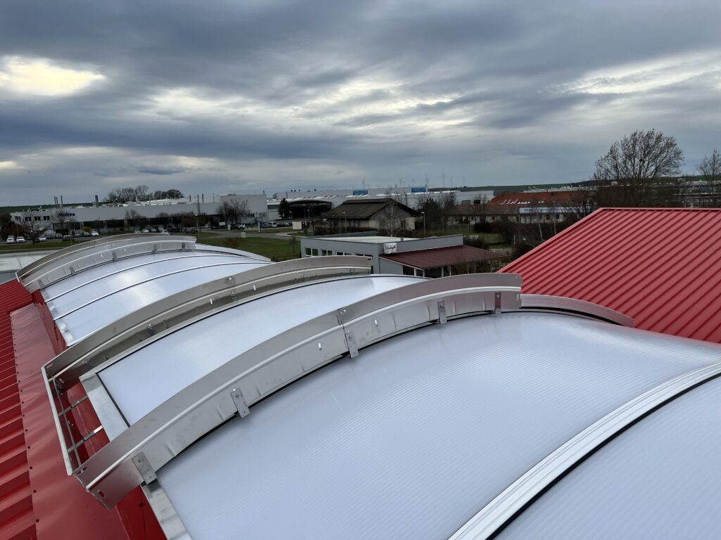 Lüftungsklappen im Firstlichtband erfüllen mit eingebauter RWA-Funktion die geforderten Brandschutzauflagen.